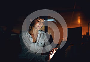 Digitizing late night work tasks. a young businesswoman using a digital tablet during a late night at work.