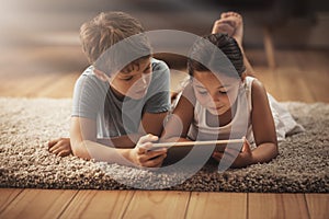 Digitizing playtime. an adorable brother and sister using a digital tablet together on the floor at home.