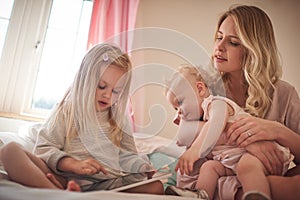 Digitizing playtime. a little girl using a digital tablet while bonding with her mother and sister on the bed.