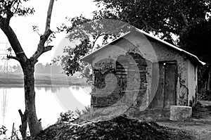 A dilapidated and abandoned hut by the river outside a village