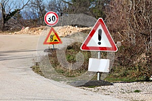 Dilapidated heavily used warning and road under construction with 30 speed limit road signs mounted on metal poles