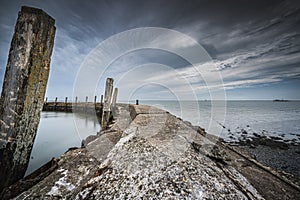 Dilapidated mooring quay in a round shape of weathered concrete with a view of the sea and a threatening cloudy sky above