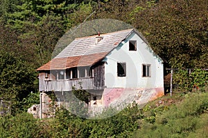 Dilapidated old family house with cracked facade and wooden balcony built on small hill surrounded with dense forest