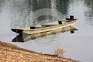 Dilapidated old light green wooden river boat made from wooden boards left next to dry grass covered river bank