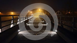 Dilapidated old pedestrian wooden bridge updated with decorative LED lights at night engulfed with thick fog and bright city photo