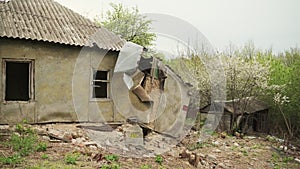 Dilapidated rural cottage on a cloudy day with overgrown vegetation. Abandoned house falling apart with nature taking