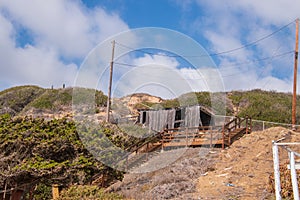 Dilapidated small building on hill with wooden staircase leading to it. Blue sky with puffy clouds