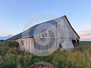 Dilapidated Wooden Barn in a Field in Illinois on a Summer Evening, with blue sky. The black roof is two-sided