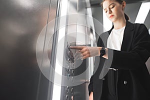 Diligent businesswoman pressing button inside elevator with a watch on her wrist. Female office worker in a black suit is pushing