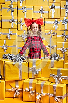 Diligent caucasian kid girl in checkered red dress among many gifts. International Women's Day birthday, holiday concept