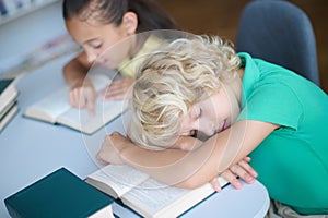 Diligent girl and exhausted sleepy boy at the library