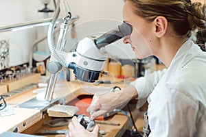 Diligent jeweler working on microscope at her workbench