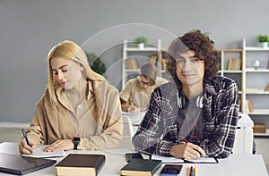 Diligent male student looking at camera sitting at desk in classroom portrait