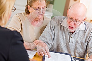 Diligent Senior Adult Couple Going Over Documents in Their Home with Agent At Signing