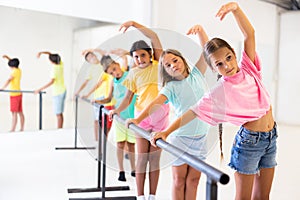 Diligent tween girl practicing classic dance moves near ballet barre