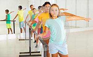 Diligent tween girl practicing classic dance moves near ballet barre