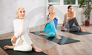 Diligent women practicing lord of the fishes pose of yoga in light fitness room