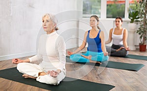 Diligent women practicing lotus pose of yoga in light fitness room