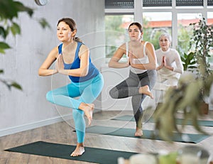 Diligent women practicing tree pose of yoga in light fitness room