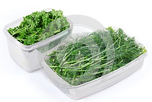 Dill and parsley twigs in two open plastic food containers