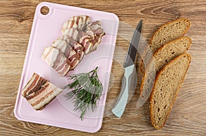 Dill, slices of salted pork lard, piece of lard on cutting board, knife, slices of bread on wooden table. Top view