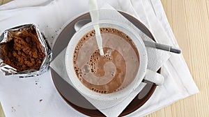 Diluted cocoa water in cup is poured with milk, beverage moves by streaks. Brown natural ingredient for making hot chocolate.