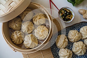 Dim sum aka dumplings,momos in a traditional bamboo steamer, with red chopsticks, Chinese cabbage & ginger root against white ba photo