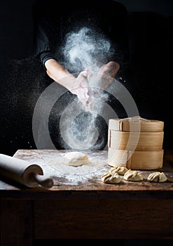 Dim sum dumplings in preparation. Male hands preparing the dough. Flour in the air motion.