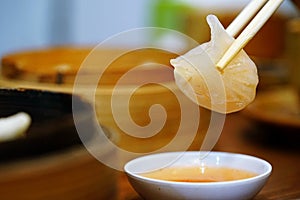 Dim Sum or Har Gow soaked with chili sauce and was picked by chopsticks over a sauce dish. popular appetizer Chinese food