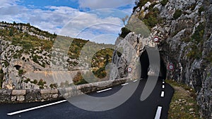 Diminishing perspective of country road D942 above canyon Gorges de la Nesque in Provence region, France with dark tunnel.