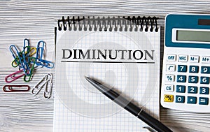 DIMINUTION - word on a notebook on a light wooden background with a calculator and a pen