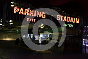 Dimly lit parking area for a stadium building with entrance and exit in neon glow signs