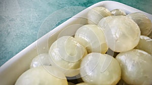 Peeled longan in a white bowl on a green background.