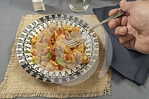 Diner taking with his fork some homemade gnocchi with tomato sauce served on a light blue plate