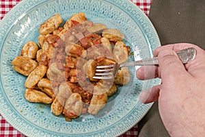 Diner taking with his fork some homemade gnocchi with tomato sauce served on a light blue plate