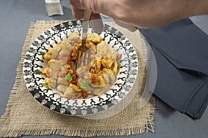 Diner taking with his fork some homemade gnocchi with tomato sauce served on a light blue plate