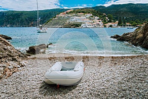 A dinghy on small hidden beach in Assos village. White yacht in Assos bay. Kefalonia Greece