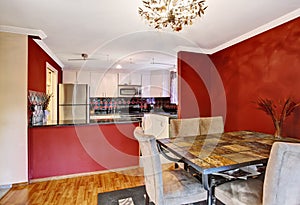 Dining area connected to kitchen with red walls, vintage chandelier.