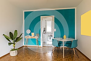 Dining room front view with small desk and turquoise wall. Open door to white kitchen and bright window