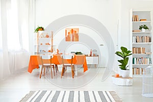 Dining room in vivid color. Orange tablecloth on table with white chairs