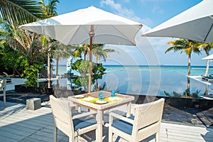 Dining setup chairs and table under umbrella near swimming pool at the tropical outdoor restaurant at island luxury resort