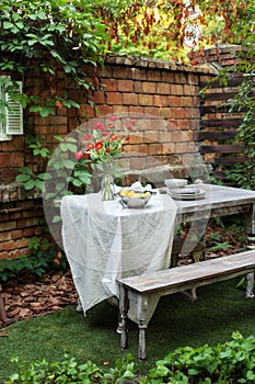 Dining table in backyard at home. Cozy space in patio or balcony. Terrace outdoor with brick wall and plants, table and  wooden be