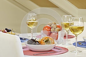 Dining table with plates full of food and fruit, red grapes, persimmons, nuts and tomatoes and crystal glasses full of white wine