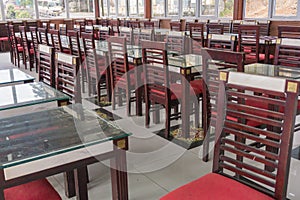 Dining table set up indoor with empty wooden chairs and glass tables, prepared for an event