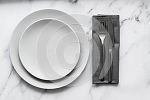 Dining table setting. Two grey plates with silver cutlery on the linen napkin
