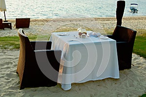 A dining table at the water edge on a tropical island, waiting for a romantic dinner to be served outdoors.