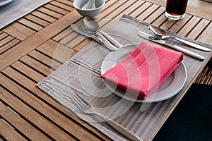 Dining wooden table set with ceramic tableware, silver utensil, red napkin and water