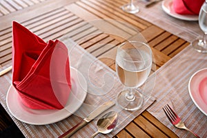 Dining wooden table set with ceramic tableware, silver utensil, red napkin and water