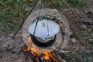 Dinner at the camp. The iron cauldron, blackened by the fire, hangs on a tripod over the fire