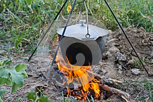 Dinner at the camp. The iron cauldron, blackened by the fire, hangs on a tripod over the fire